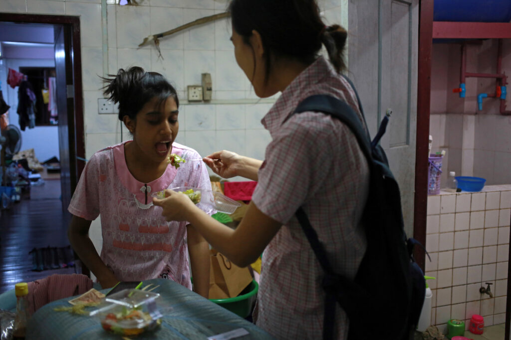 Phway Phway (R, Christian) feed her friend Thwe Thwe Oo (L, Christian) in the kitchen.