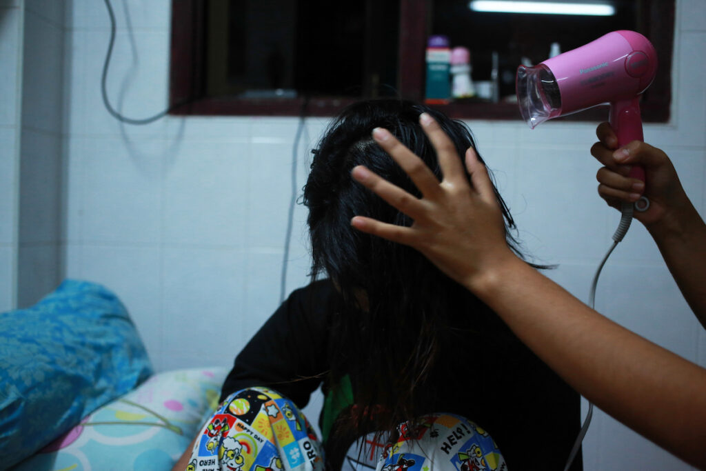 Khin Zar Mon (R, Muslim) helps Pa Pa Phyo (L, Buddhist) to dry her wet hair with dryer in the living room.